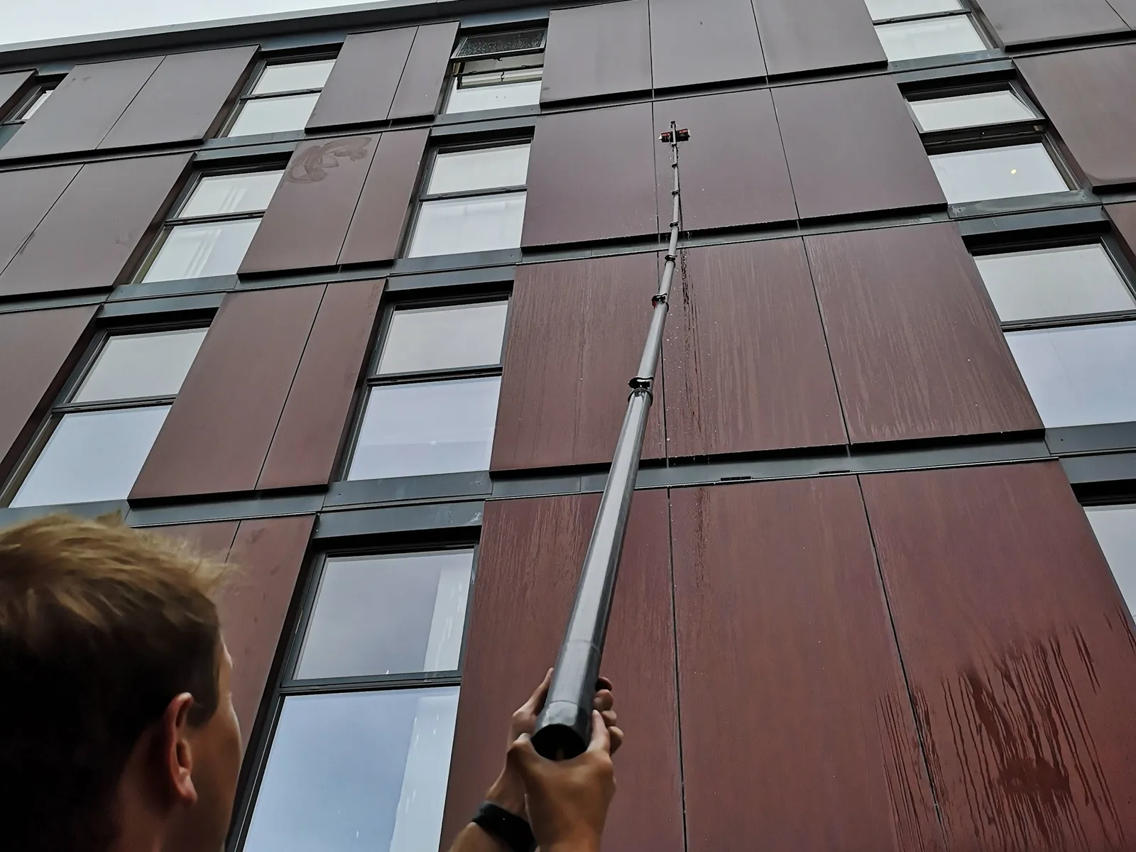 Apartment block cleaning: an operative cleaning the windows with a water-fed pole