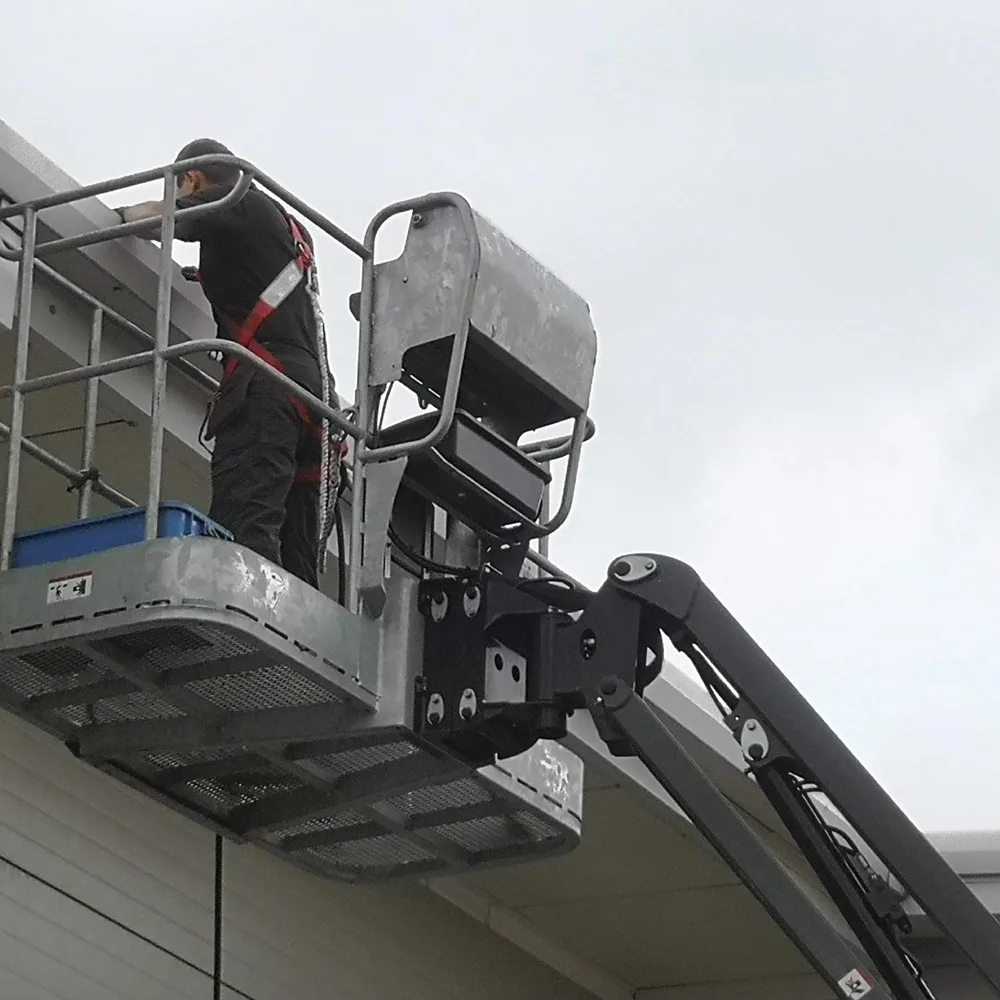 Operative working from a cherry picker basket at a building's roofline