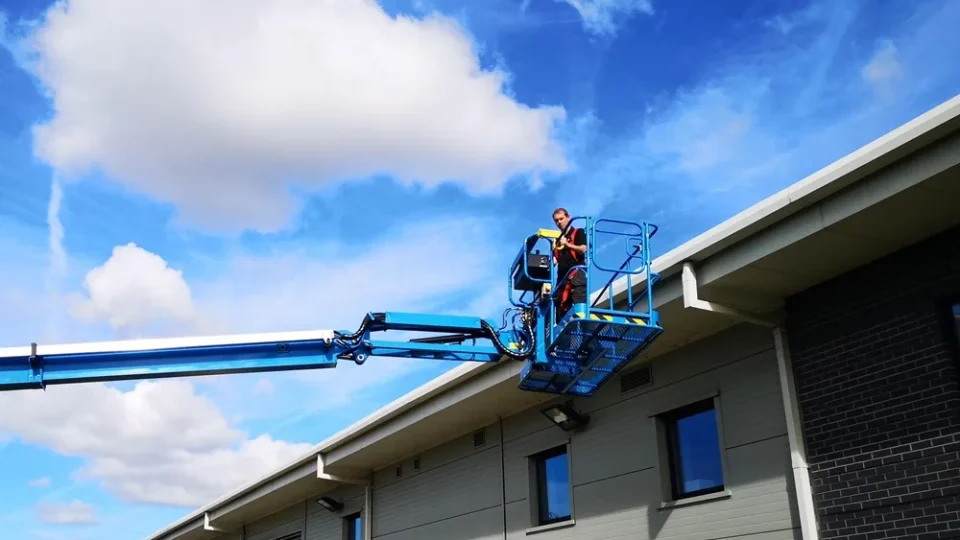 Operative in a cherry picker basket at the roofline of a commercial building
