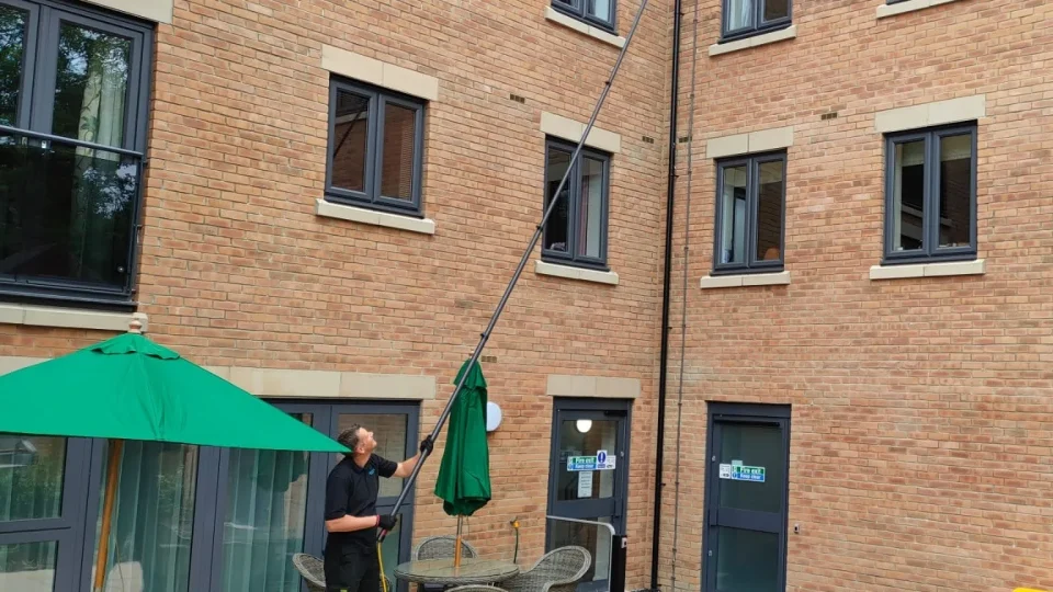 Operative cleaning upper windows above a courtyard terrace with a water-fed pole