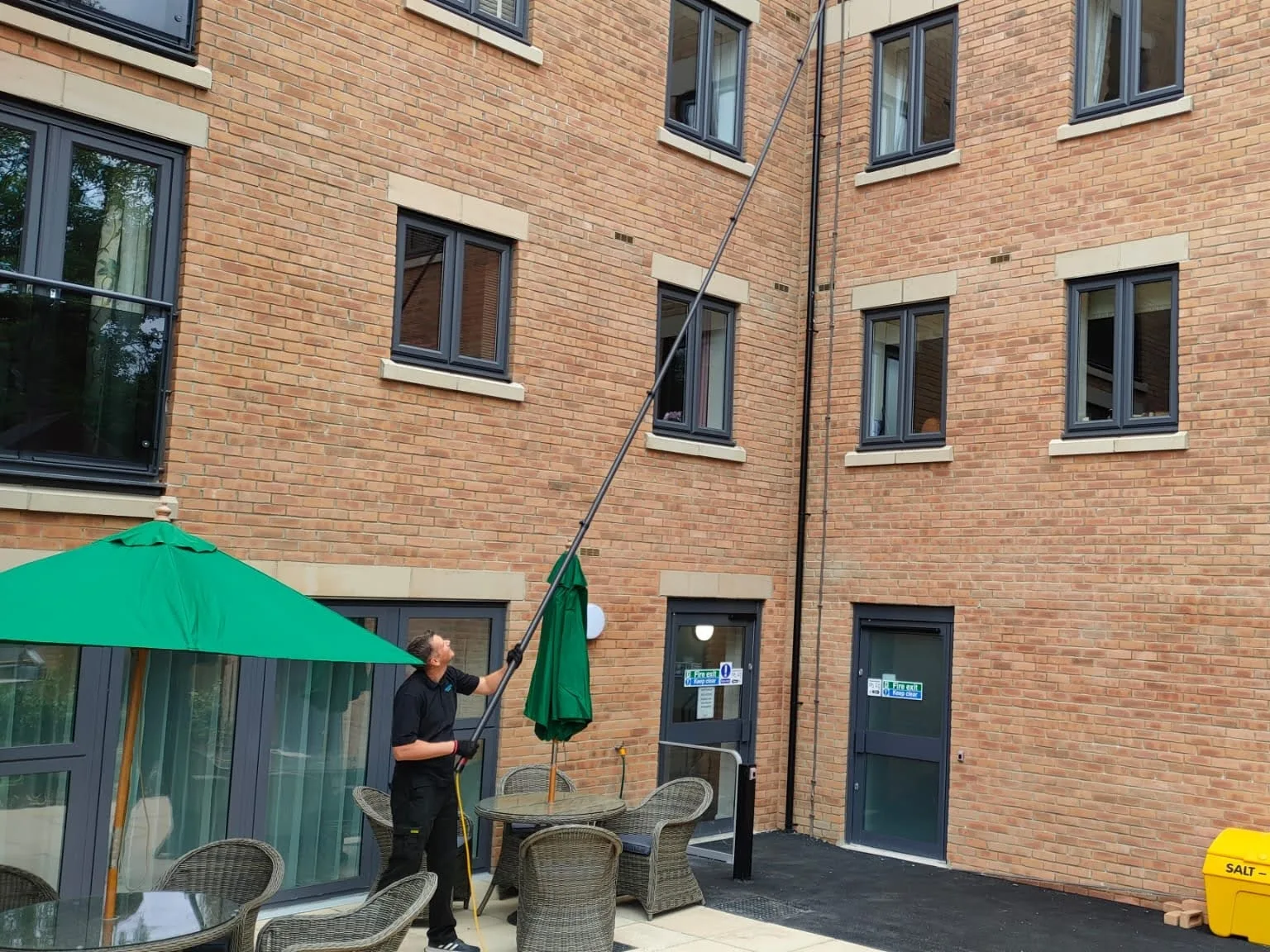 Operative cleaning upper windows above a courtyard terrace with a water-fed pole