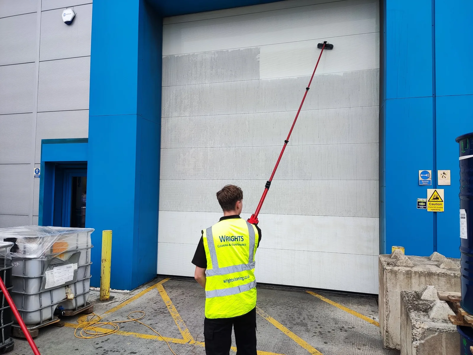 Operative cleaning a large industrial door with a water-fed pole