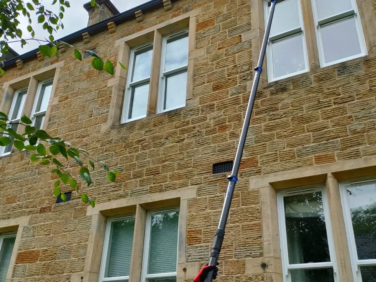 Water-fed pole cleaning the sash windows of a stone-built building