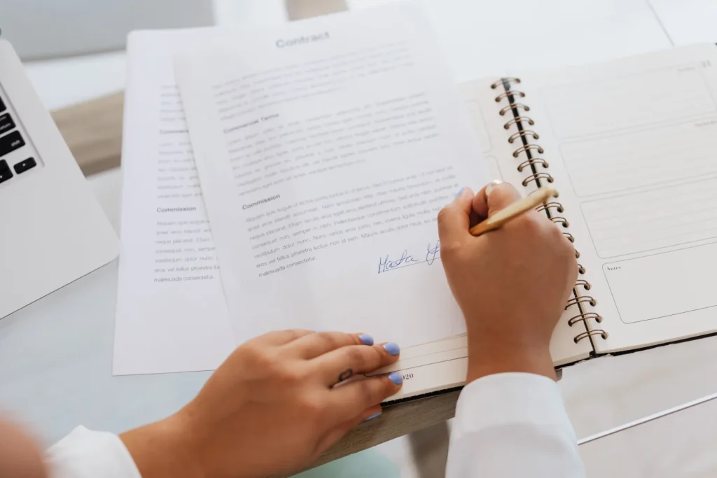 Hands signing a printed contract at an office desk