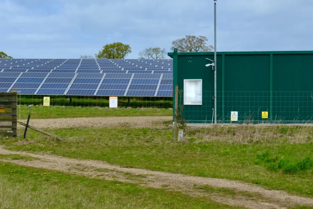 Rows of ground-mounted solar panels on a solar farm beside a green equipment hut