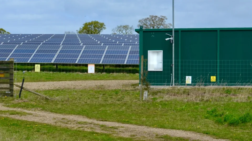 Rows of ground-mounted solar panels on a solar farm beside a green equipment hut