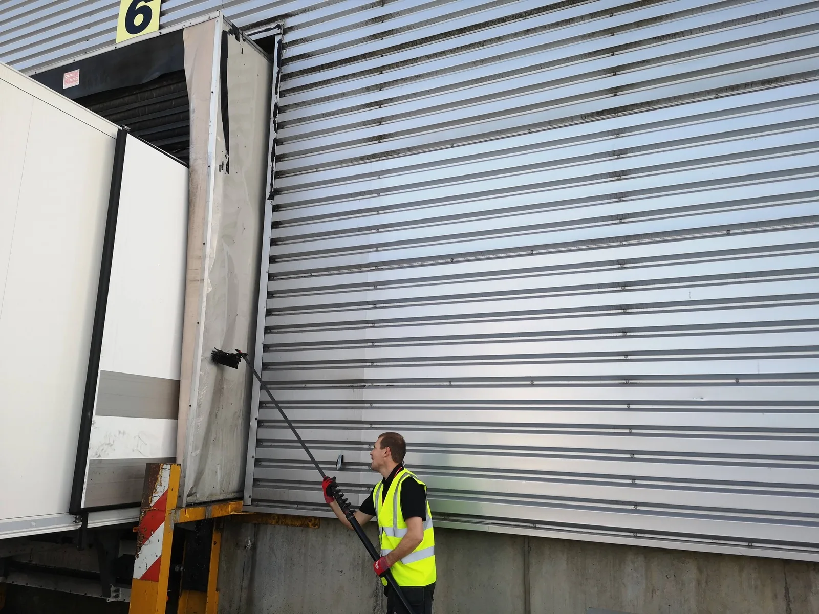 Operative cleaning warehouse cladding beside a loading bay with a water-fed pole