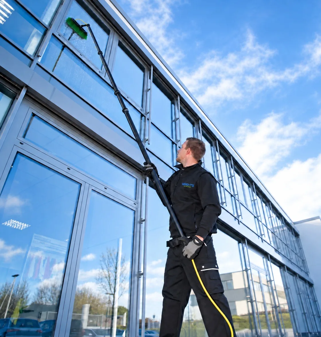 Commercial window cleaning: a Wrights Cleaning operative cleaning the upper glazing of a modern office with a water-fed pole